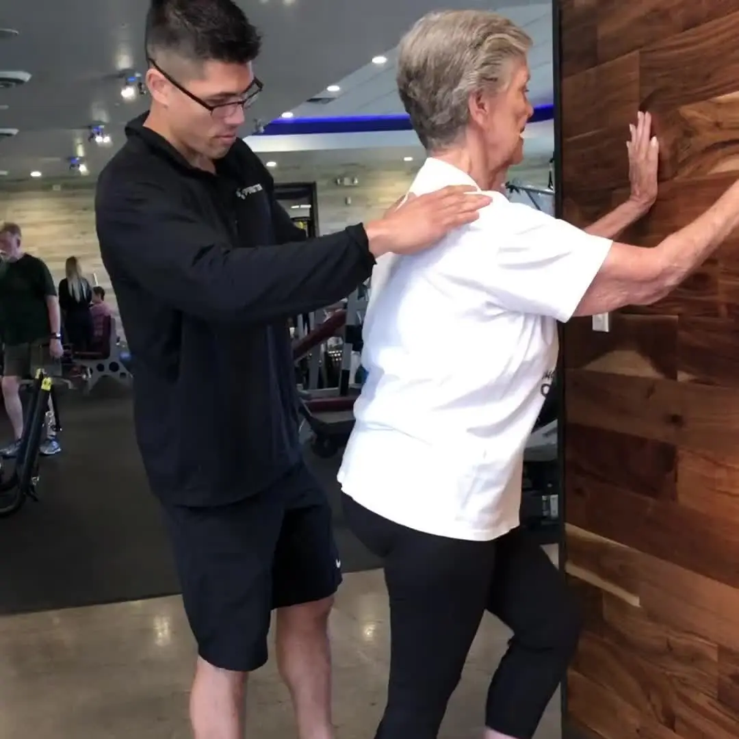 A Prestige Fitness posture specialist assessing a standing client's shoulder and trunk alignment in the club
